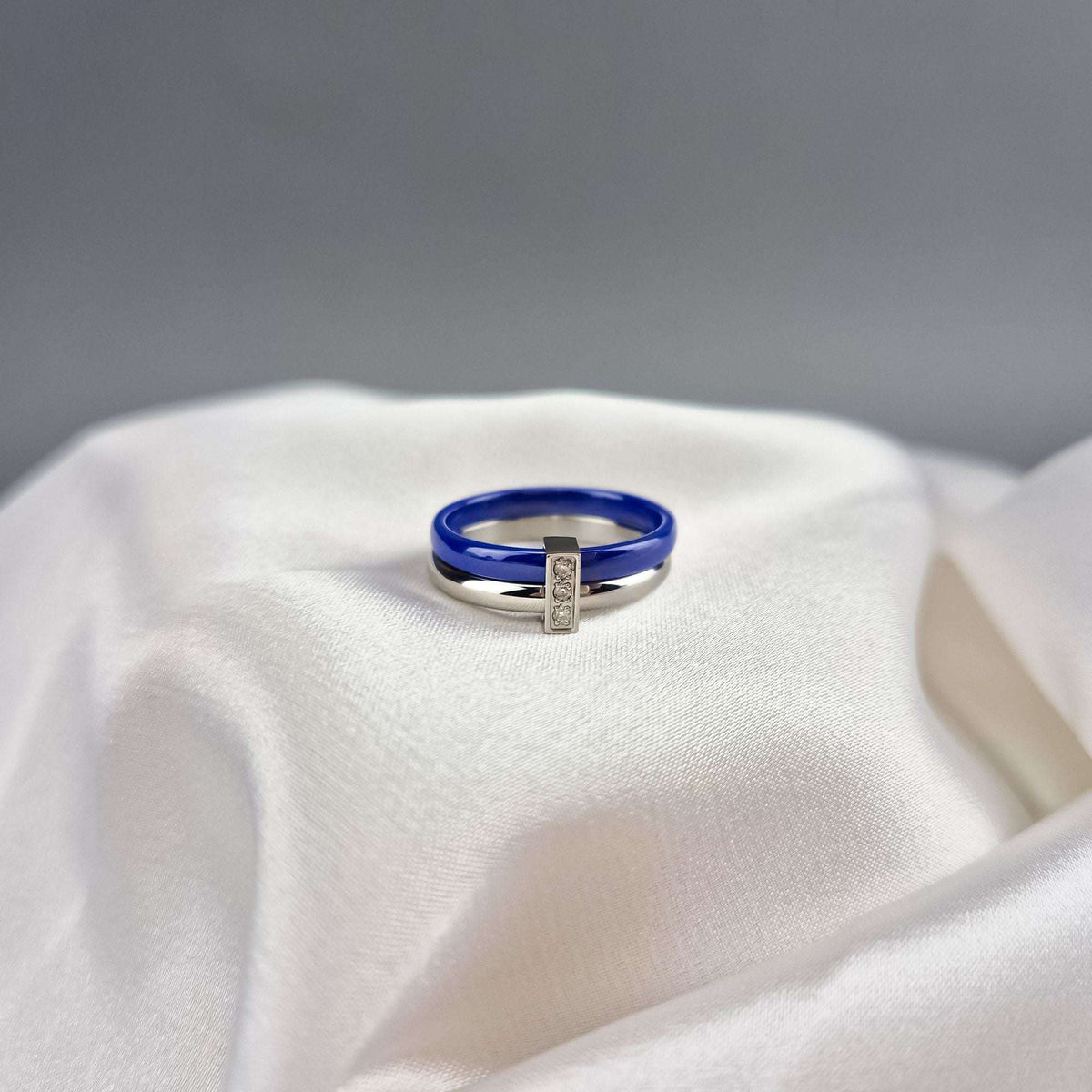 Blue ceramic ring with a silver-tone zirconia band on silk drapery