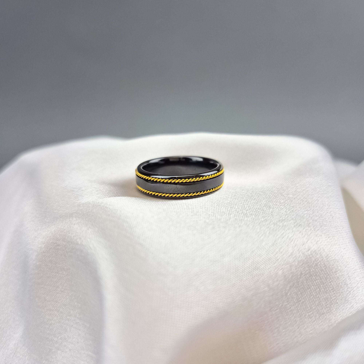 Black ceramic ring with gold-tone twisted strands shot from above on silk