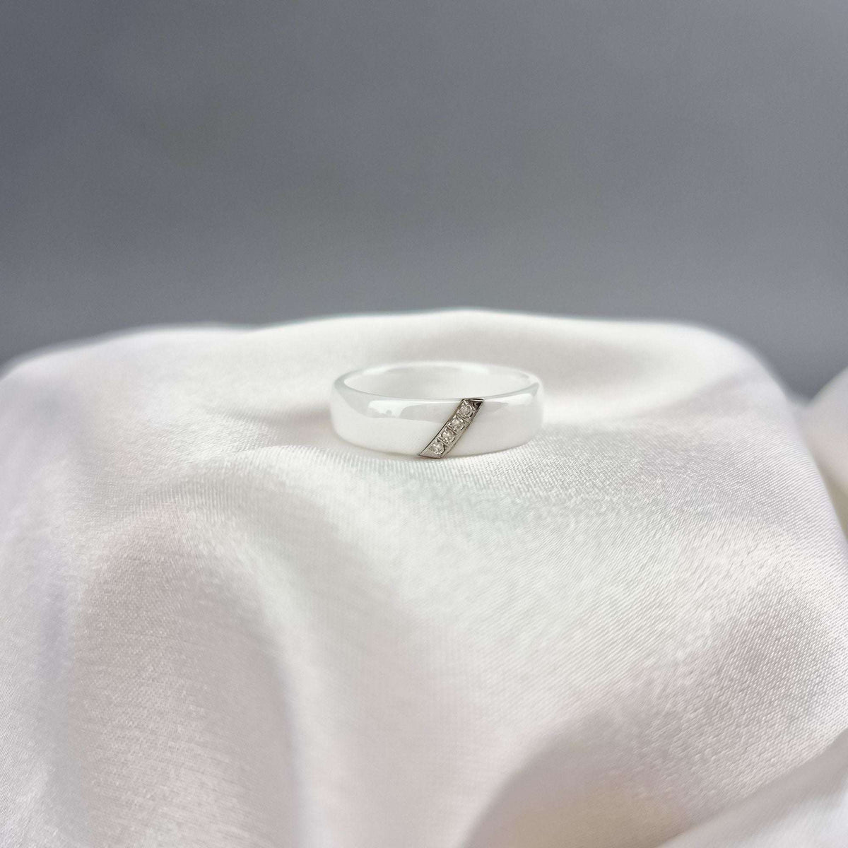 White ceramic ring with a slanted silver-tone cubic zirconia strip on silk