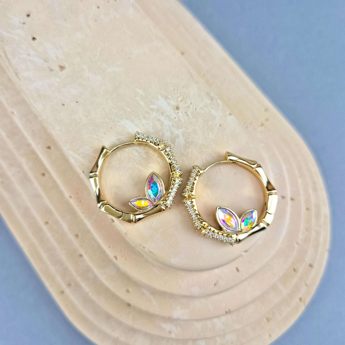 Pair of gold-tone hoop earrings with multicoloured crystals on a beige stand