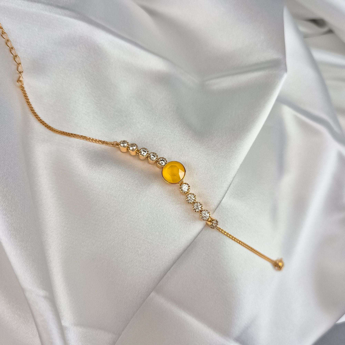 Gold-plated bracelet with a faceted yellow crystal and cubic zirconia on white satin