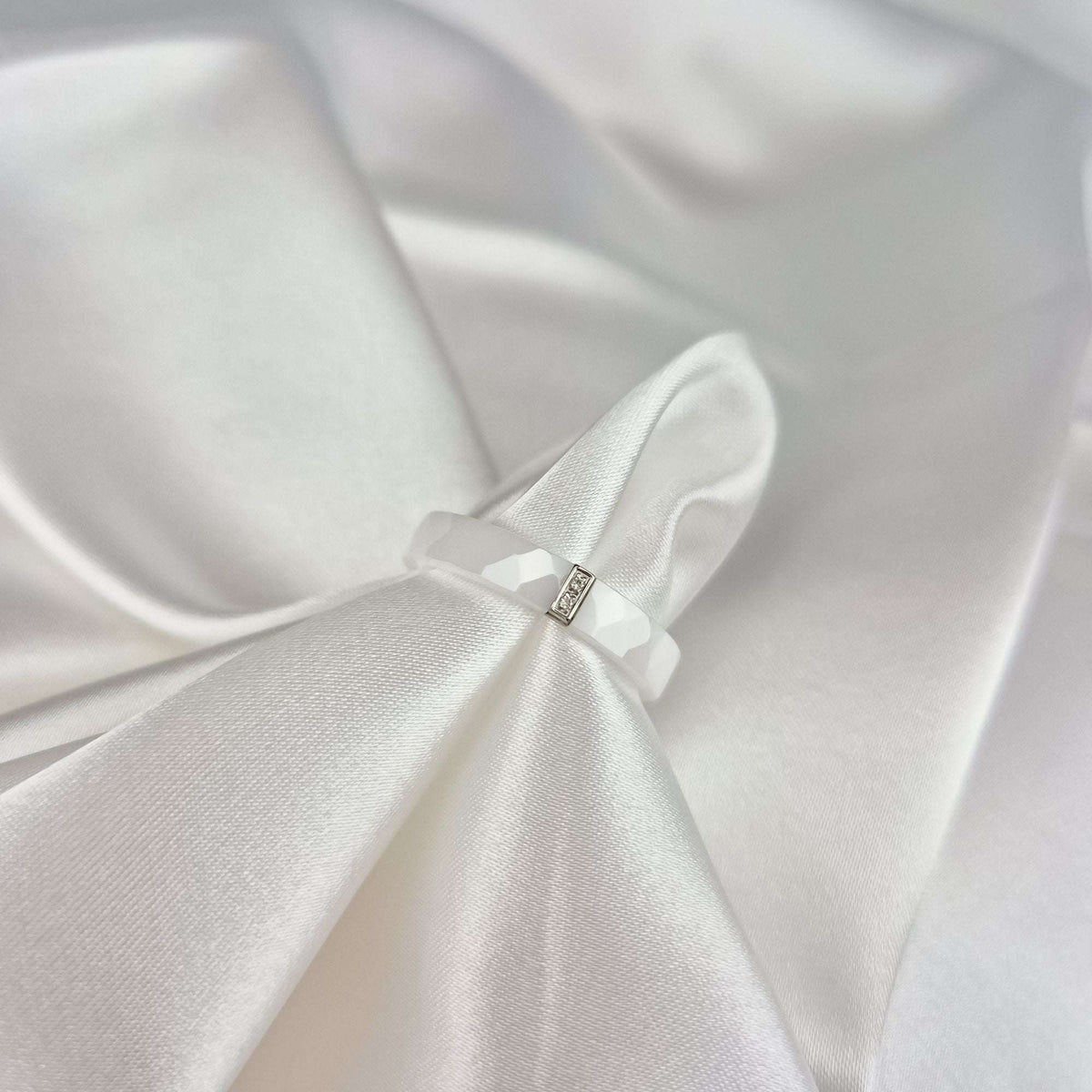 Close-up of the white ceramic ring on folds of shiny silk