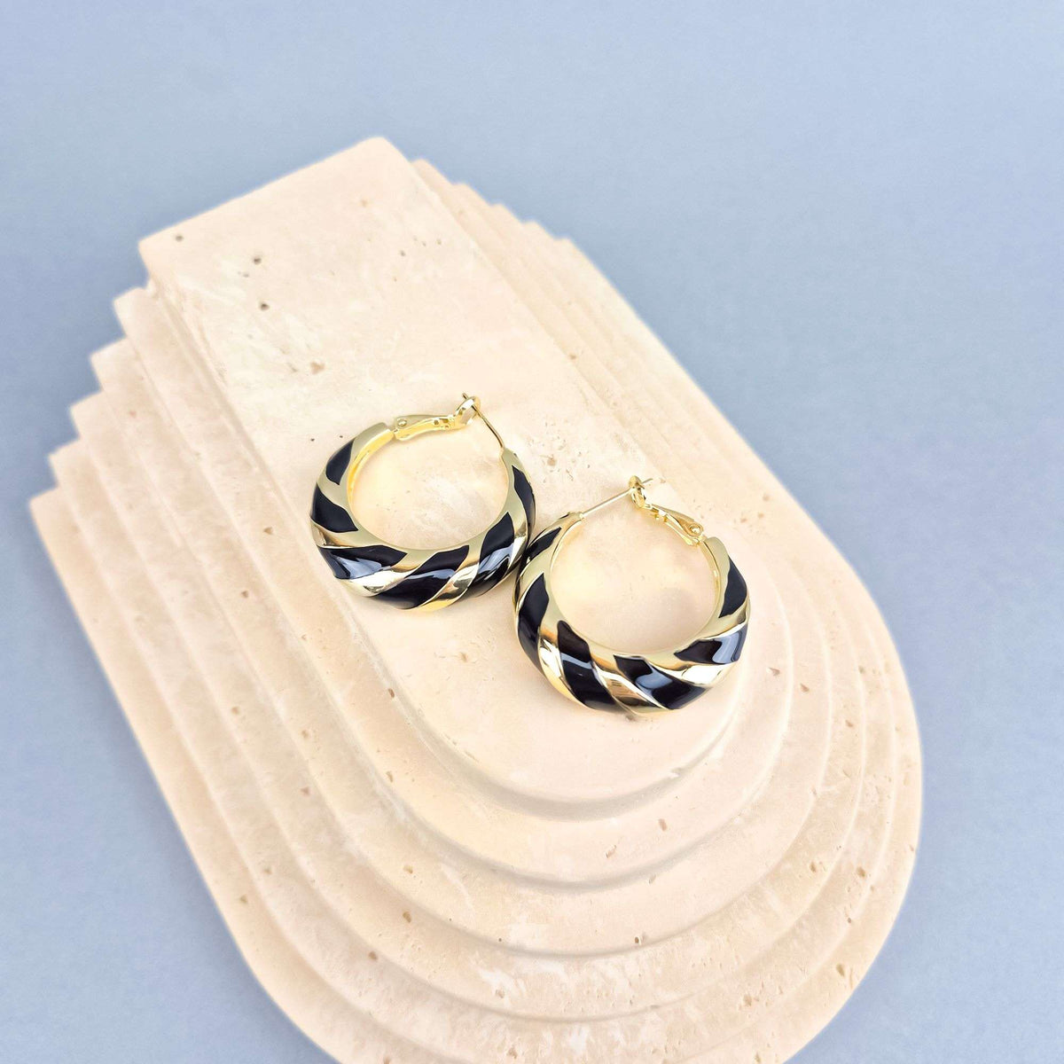 Black and gold-tone striped round earrings on a sand-coloured stone stand