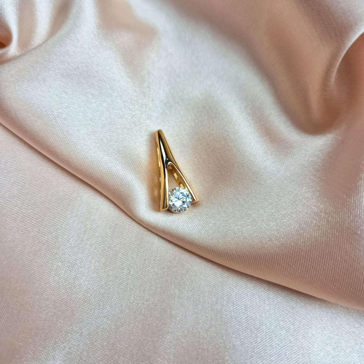 Gold-tone pendant with a clear stone lying on cream silk