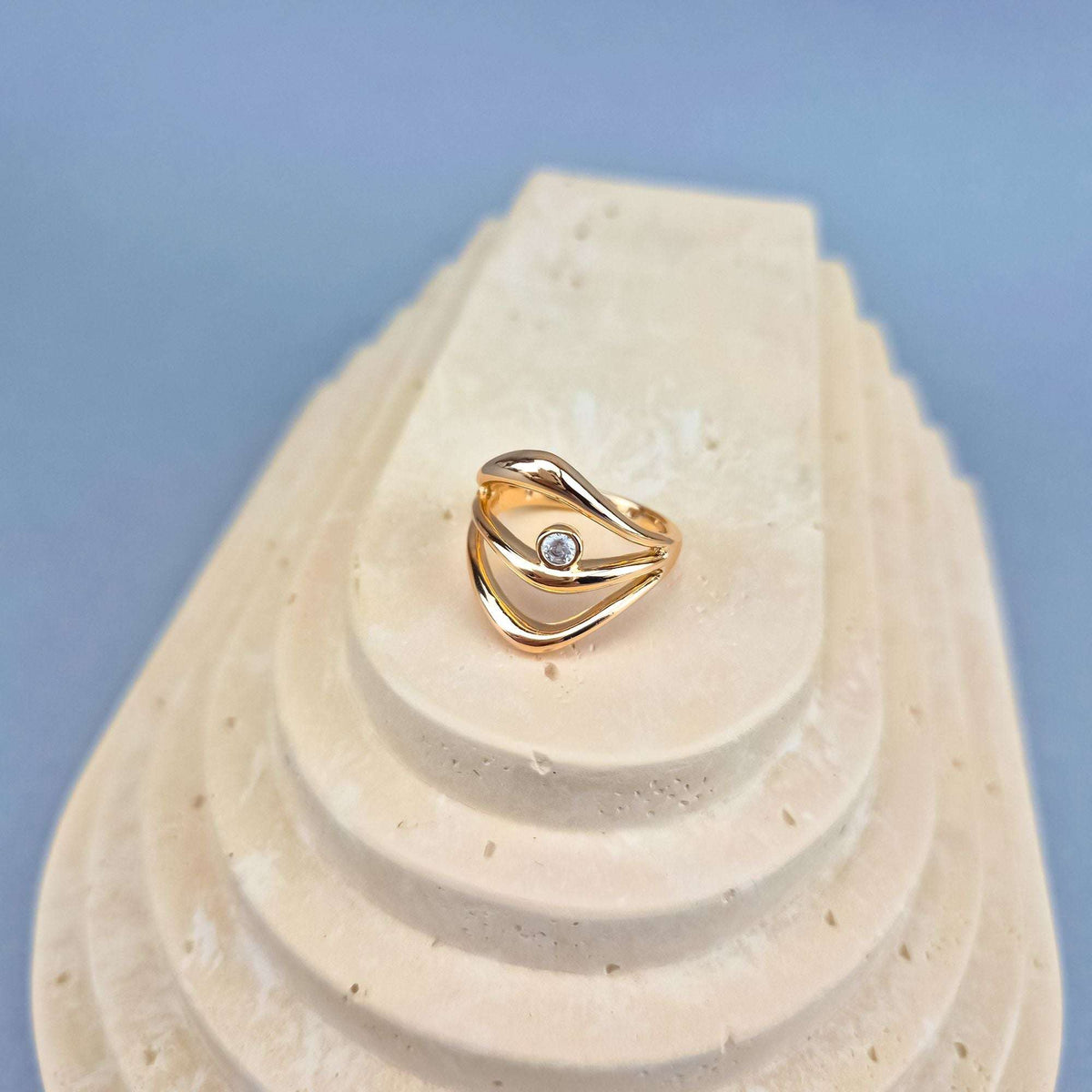 Gold-plated ring with a white stone on a pale stone stand, blue background