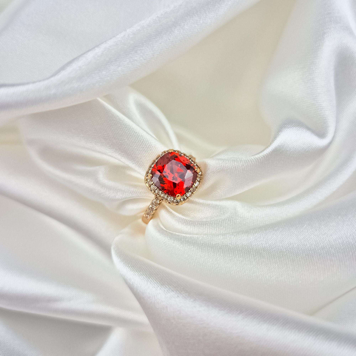 Close-up of the red stone halo ring on white satin