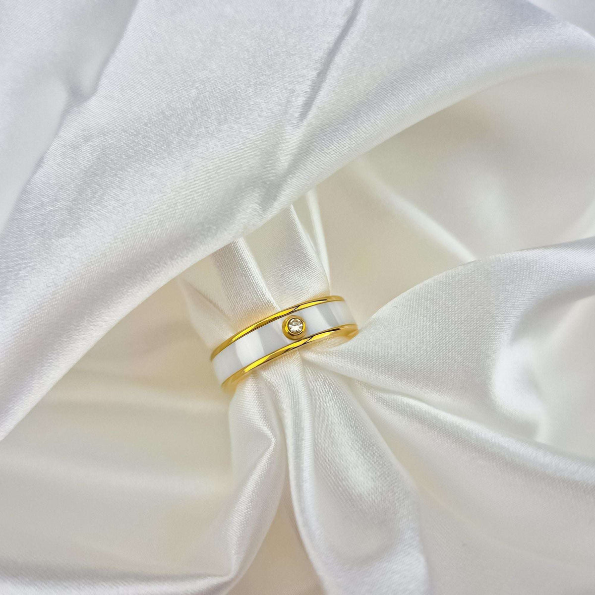 White ceramic band ring with a tiny cubic zirconia on white silk drapery