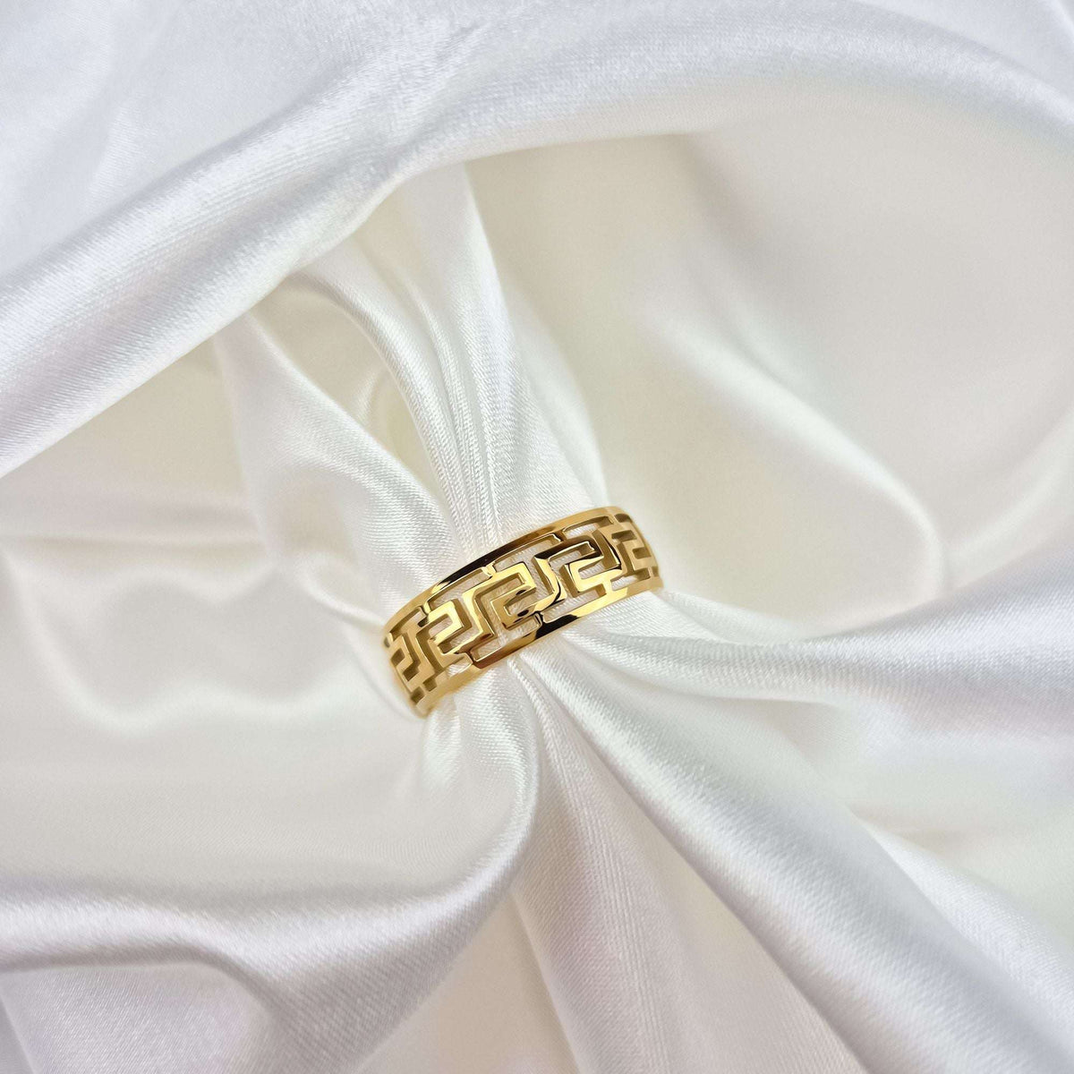 Close-up of the gold-plated meander ring on white satin, openwork visible