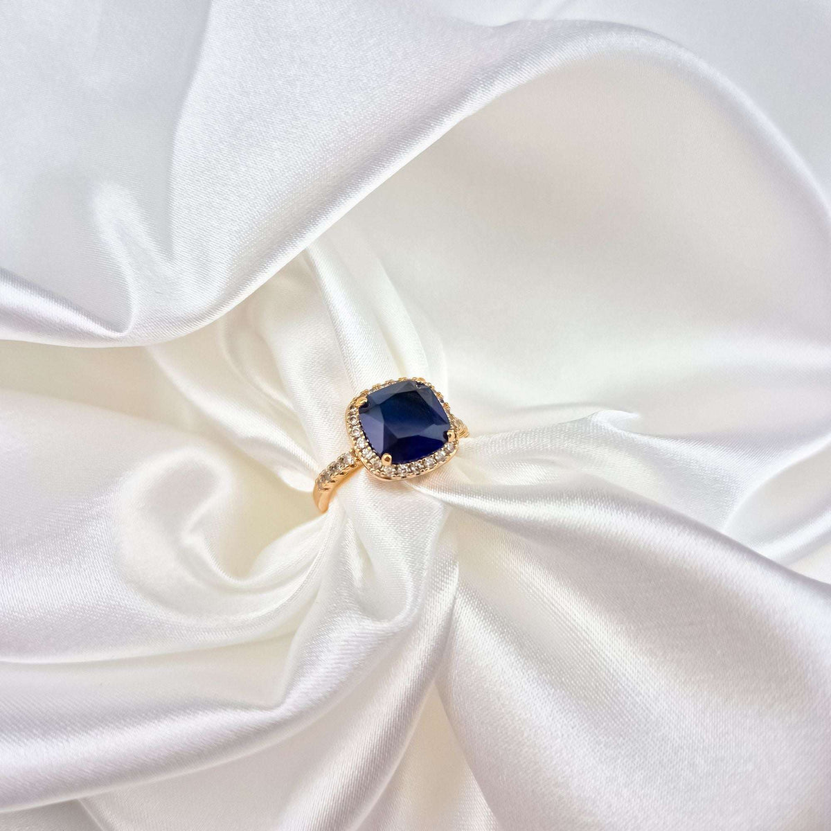 Dark blue stone ring in a cubic zirconia frame on white satin