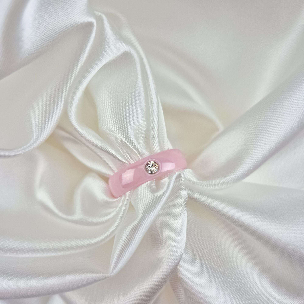 Smooth pink ceramic ring with a clear cubic zirconia on white satin