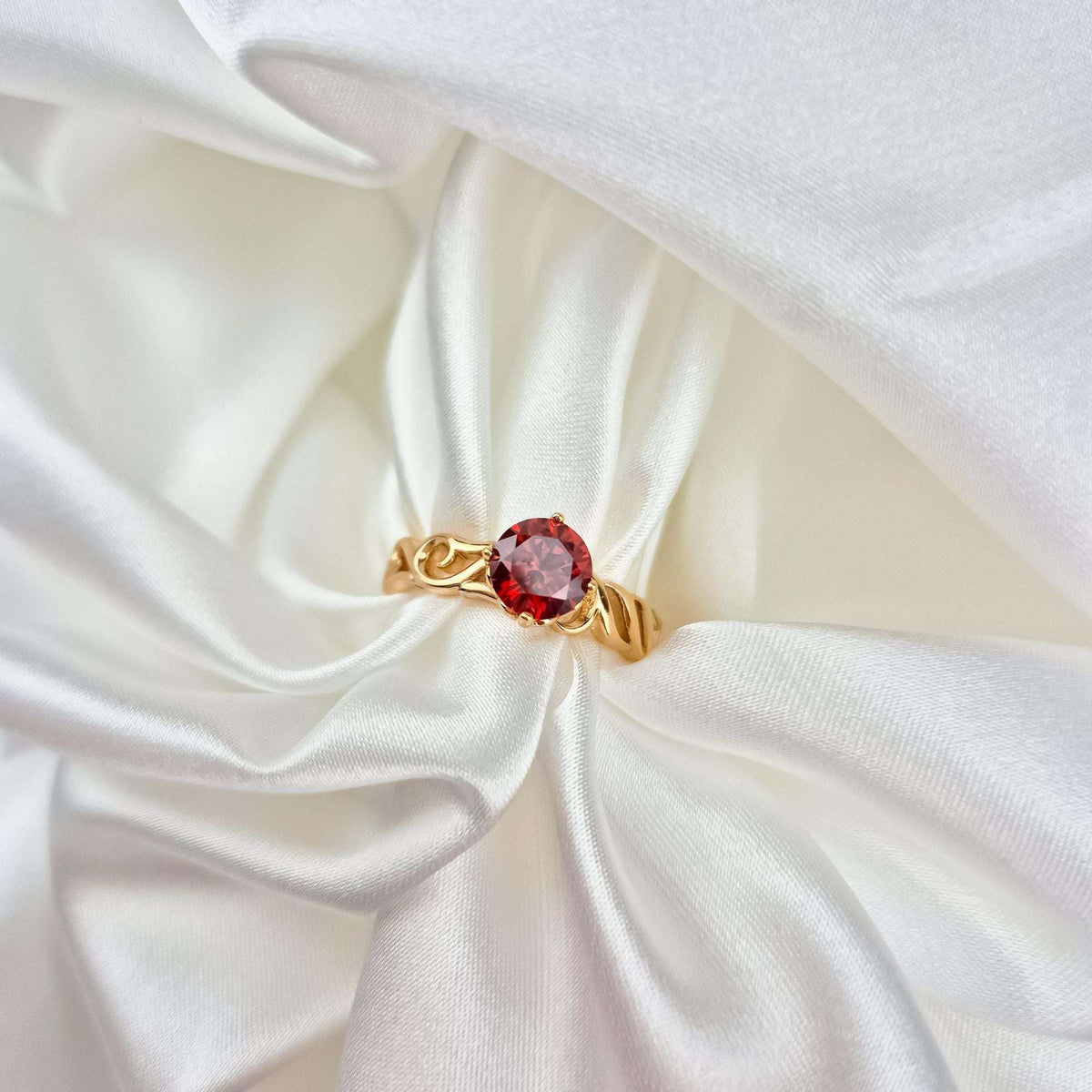 Gold-plated ring with a round red cubic zirconia on white satin