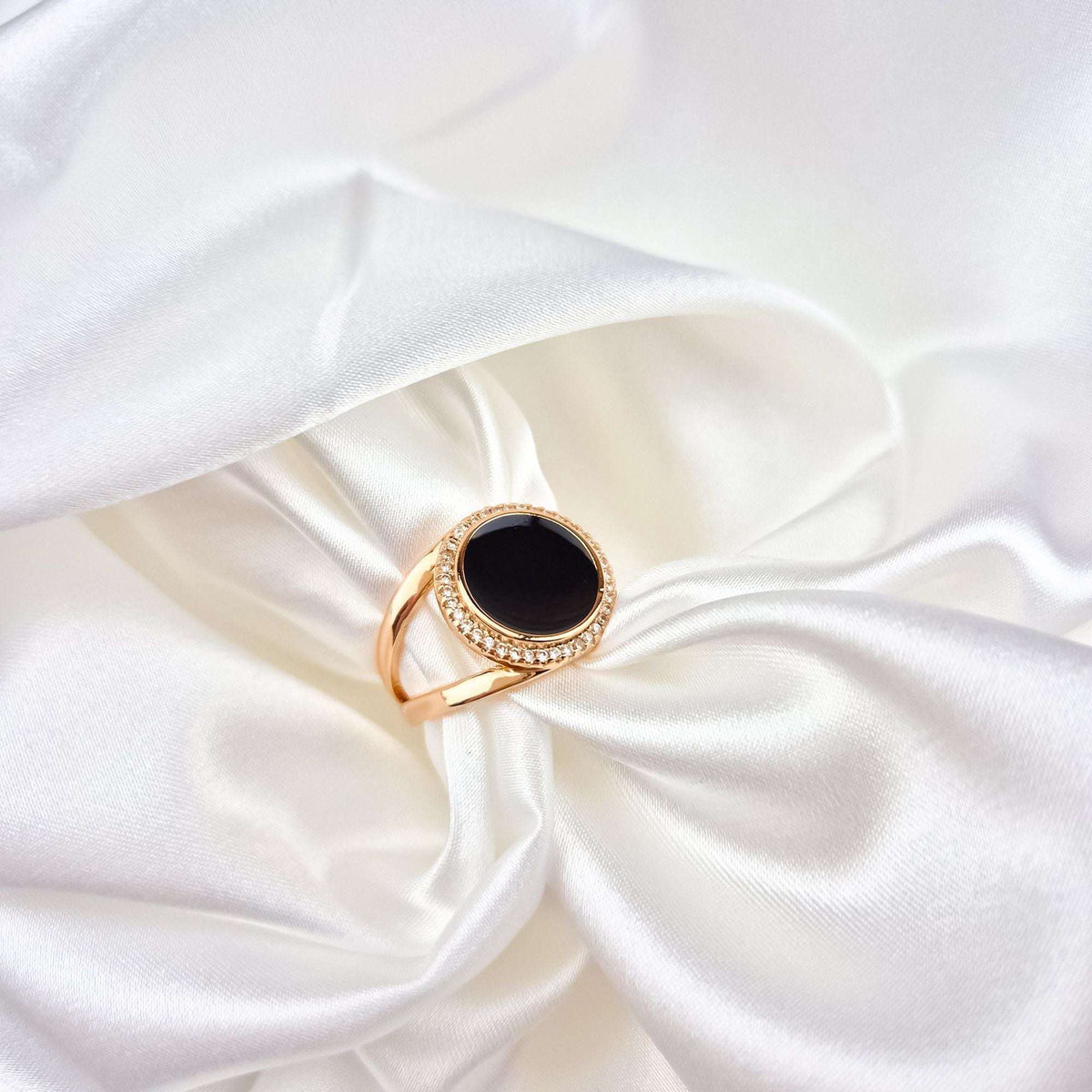 Oval gold-plated ring with black enamel and a sparkling stone frame on white silk