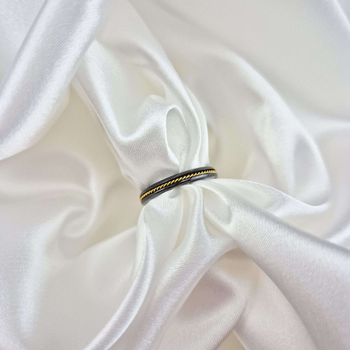 Black ceramic ring with a gold-tone twist standing on white satin