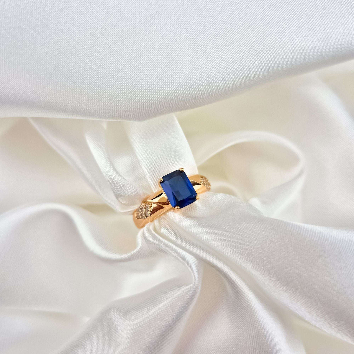 Close-up of the gold-plated ring with a blue rectangular stone on white satin