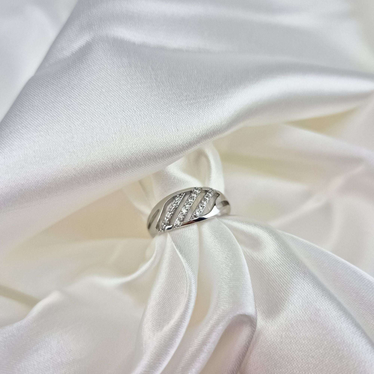 Close-up of the silver-tone ring with three sparkling bands on white silk