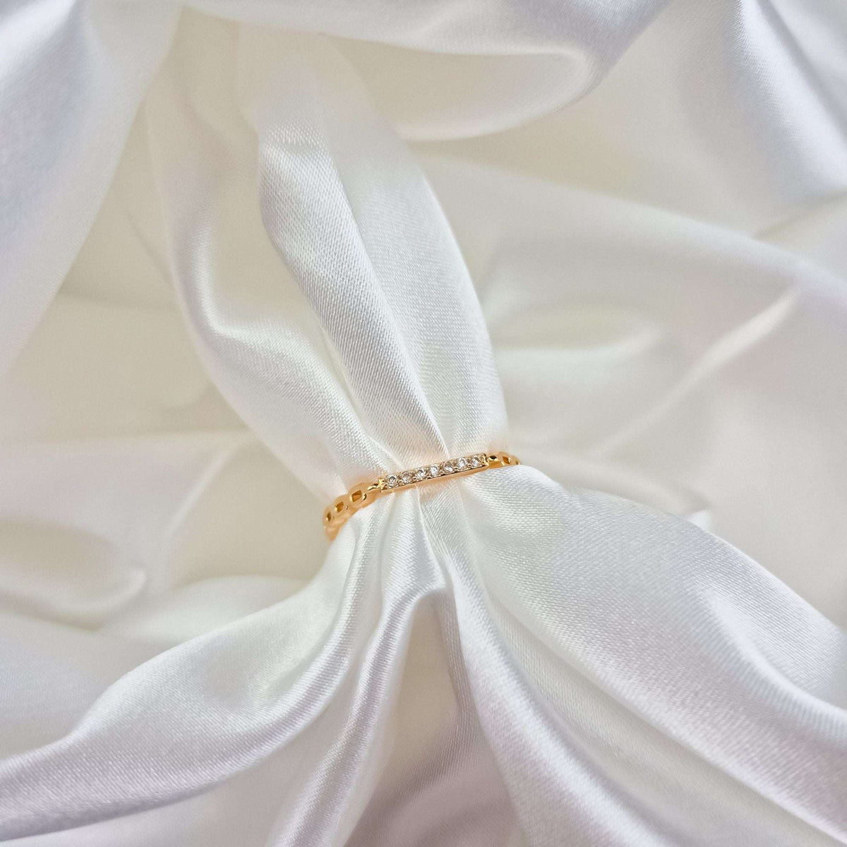 Slim gold-plated ring with tiny white cubic zirconia on white satin