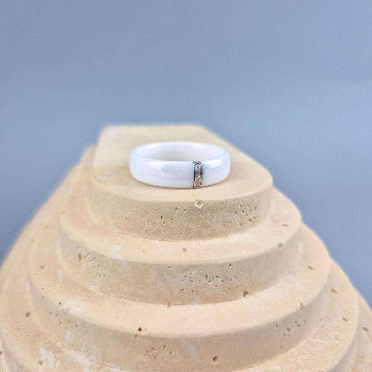 Ceramic ring with a cubic zirconia strip on a pale stone step, blue-grey background
