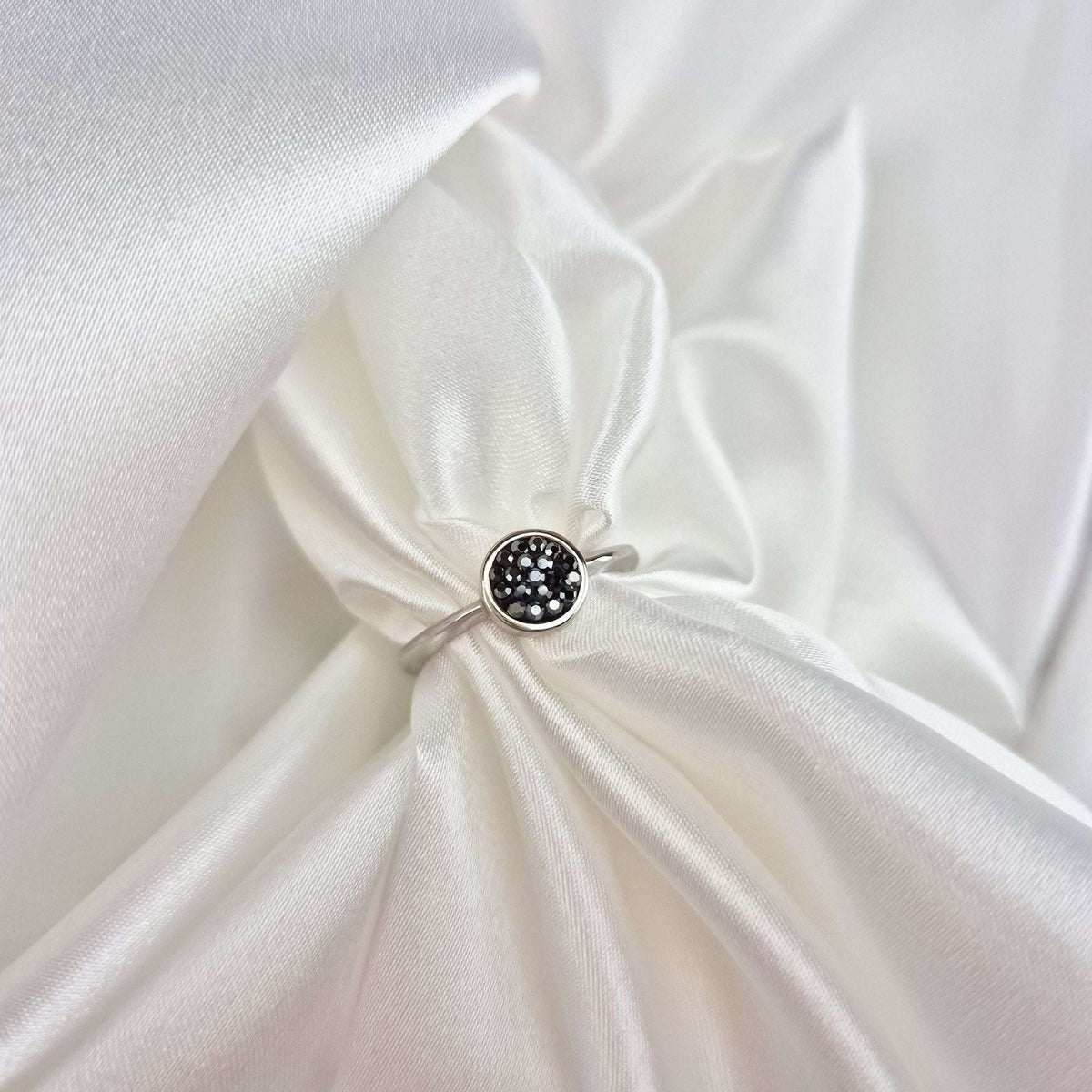 Fine silver-tone ring with a sparkling black crystal disc on white satin