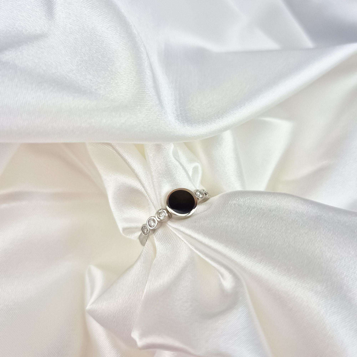 Black disc ring with white side stones photographed on cream satin fabric