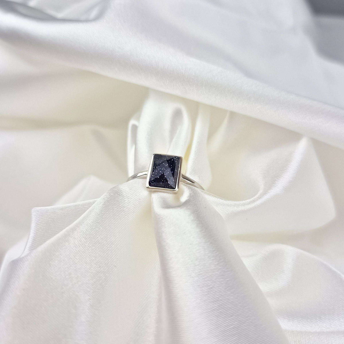 Silver-tone ring with a blue stone lying on white satin fabric