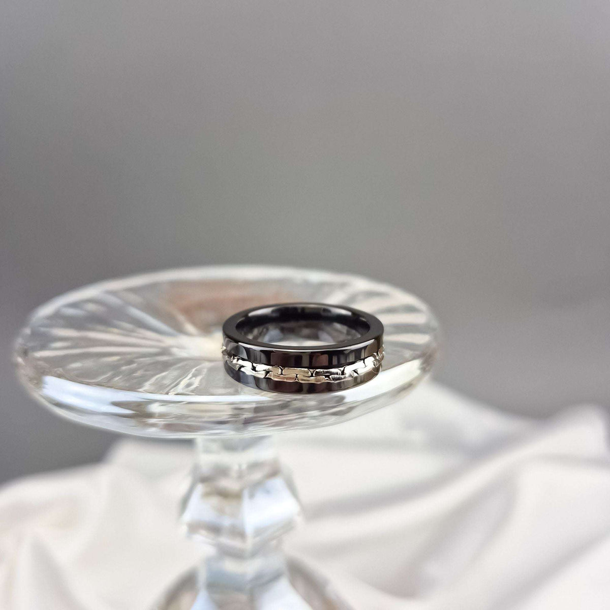 Black ceramic ring on a crystal stand, close-up of the shiny chain inlay