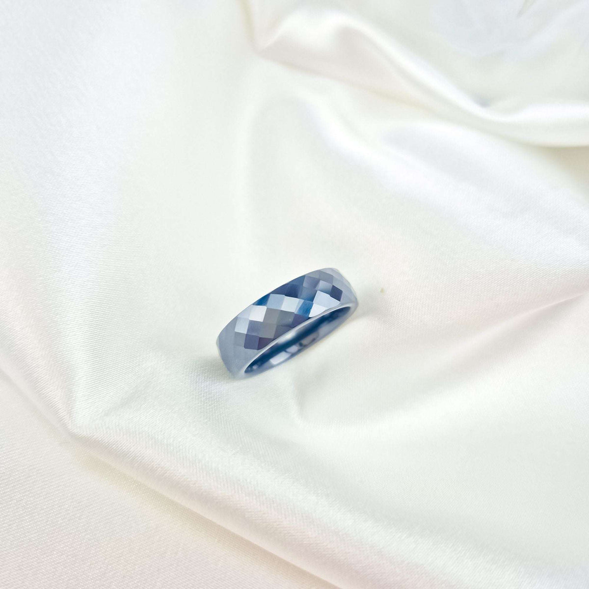 Faceted blue ceramic ring in close-up on creamy white satin