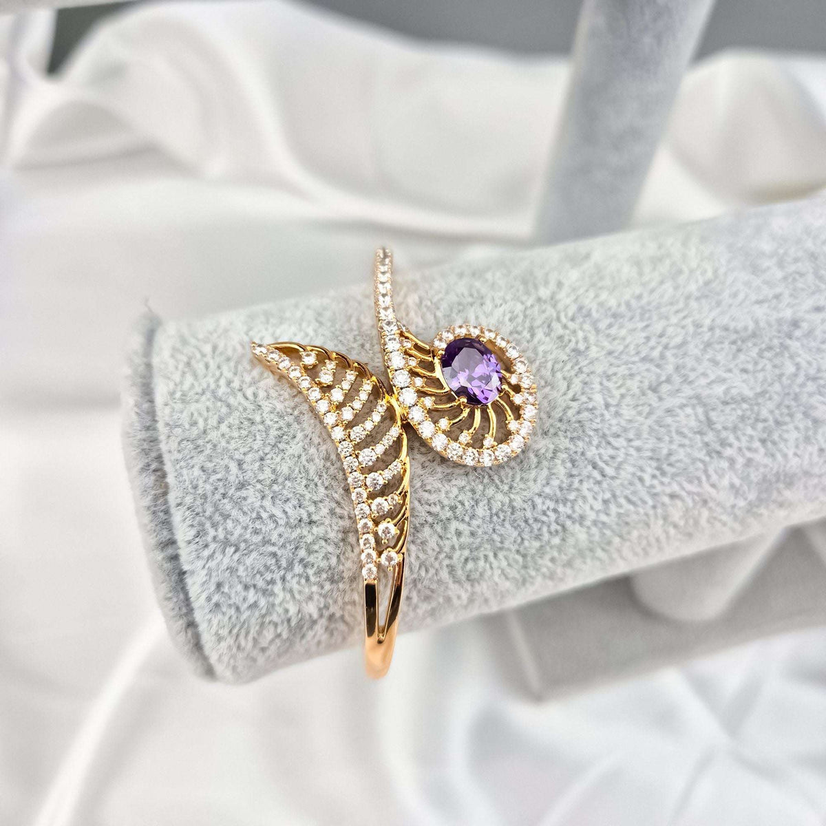Gold-plated spiral bracelet with a violet stone and crystals on a display cushion