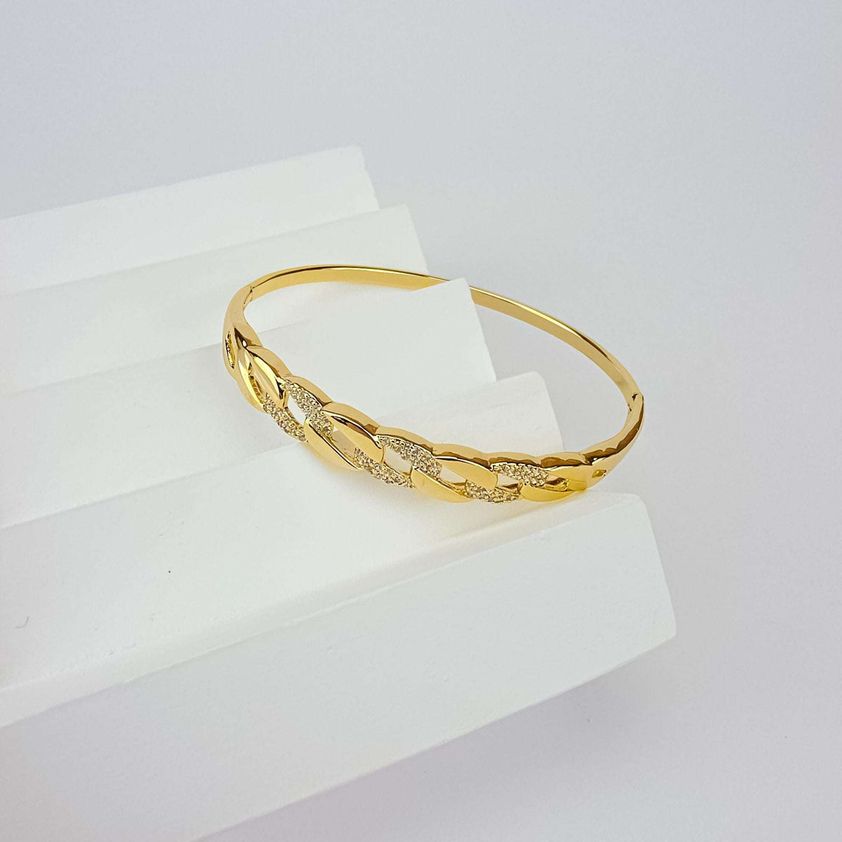 Gold-tone chain-link bangle with sparkling cubic zirconia on a white stand