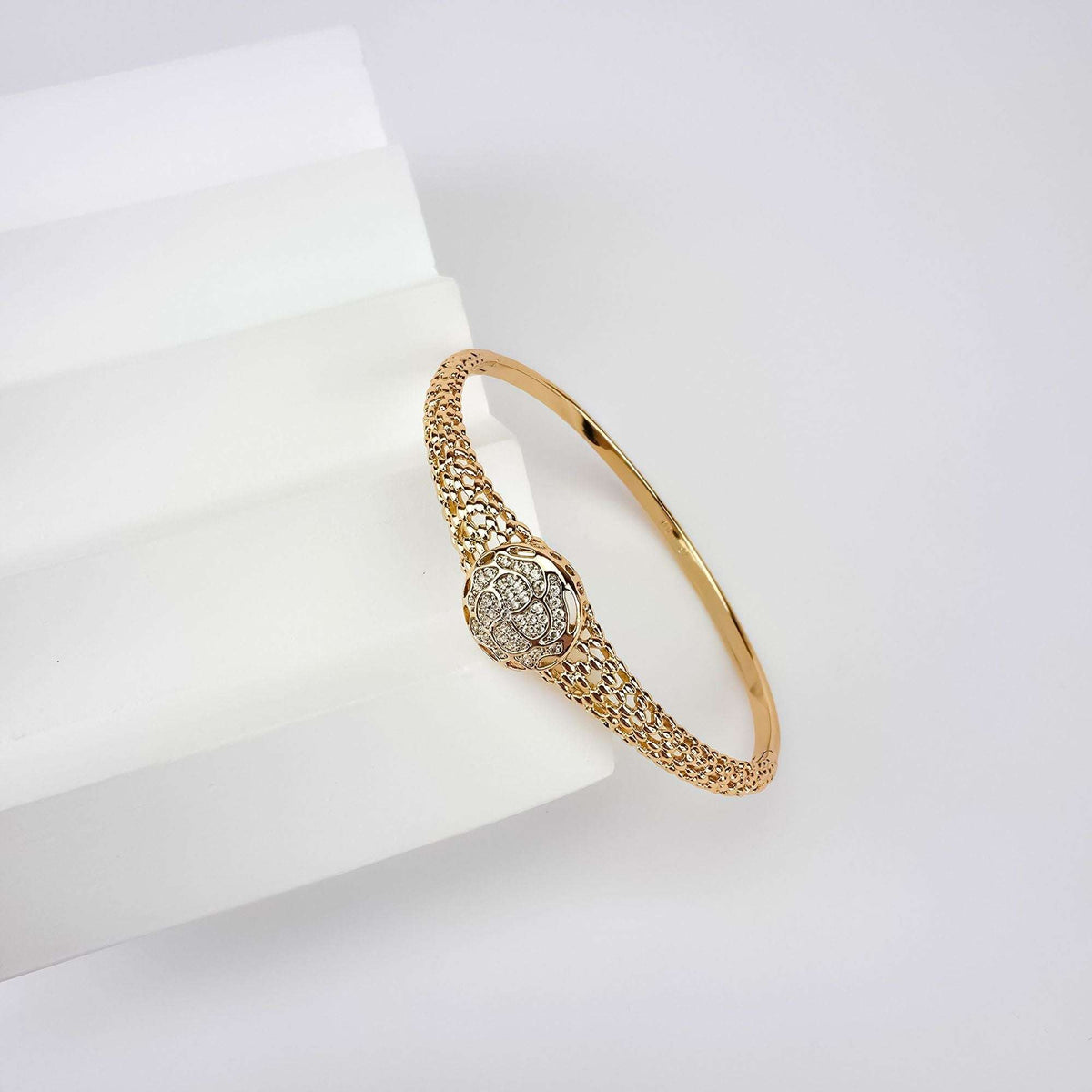 Gold-tone mesh bangle on a white block with a sparkling rose medallion