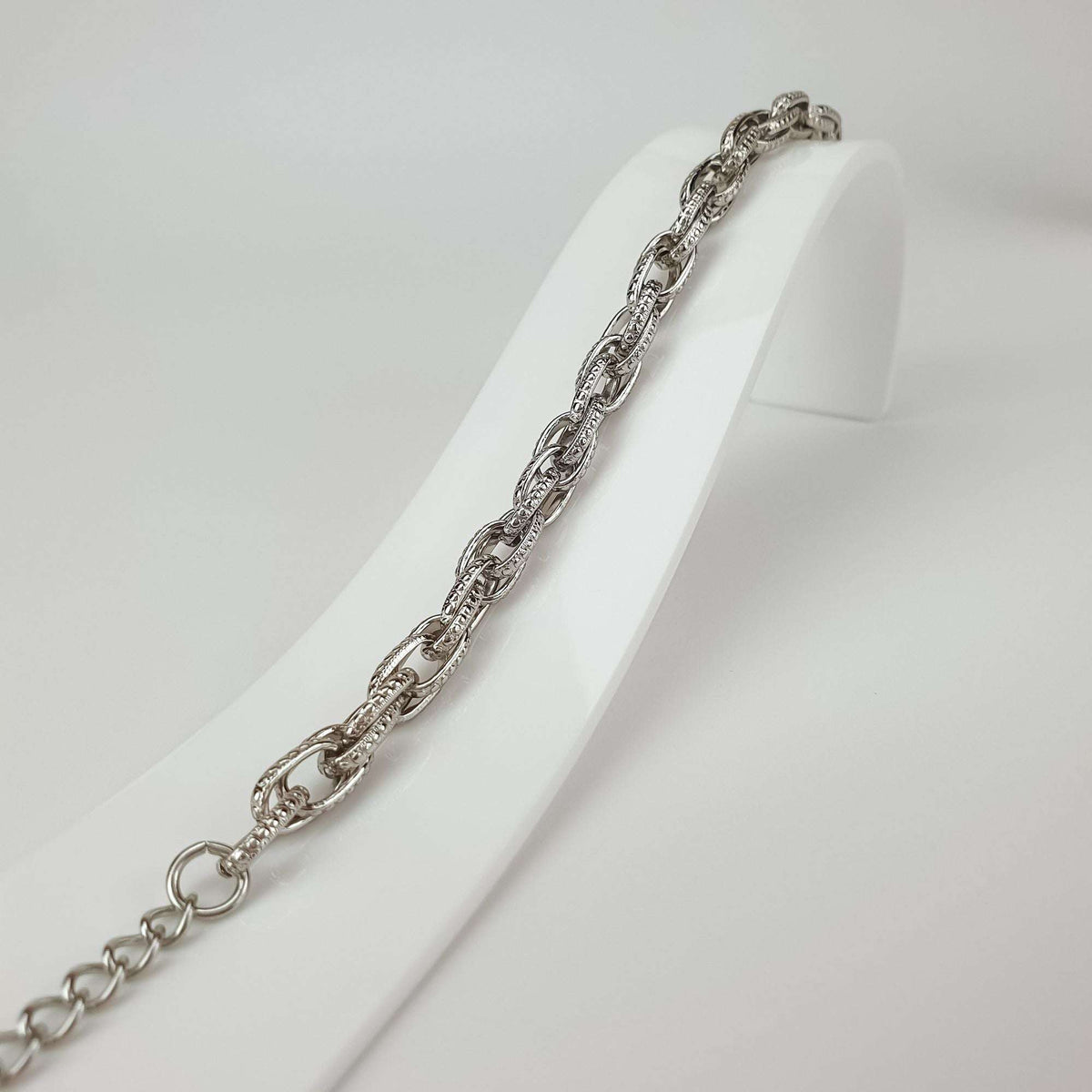 Close-up of the bracelet on a white stand, fine grained link pattern and extender