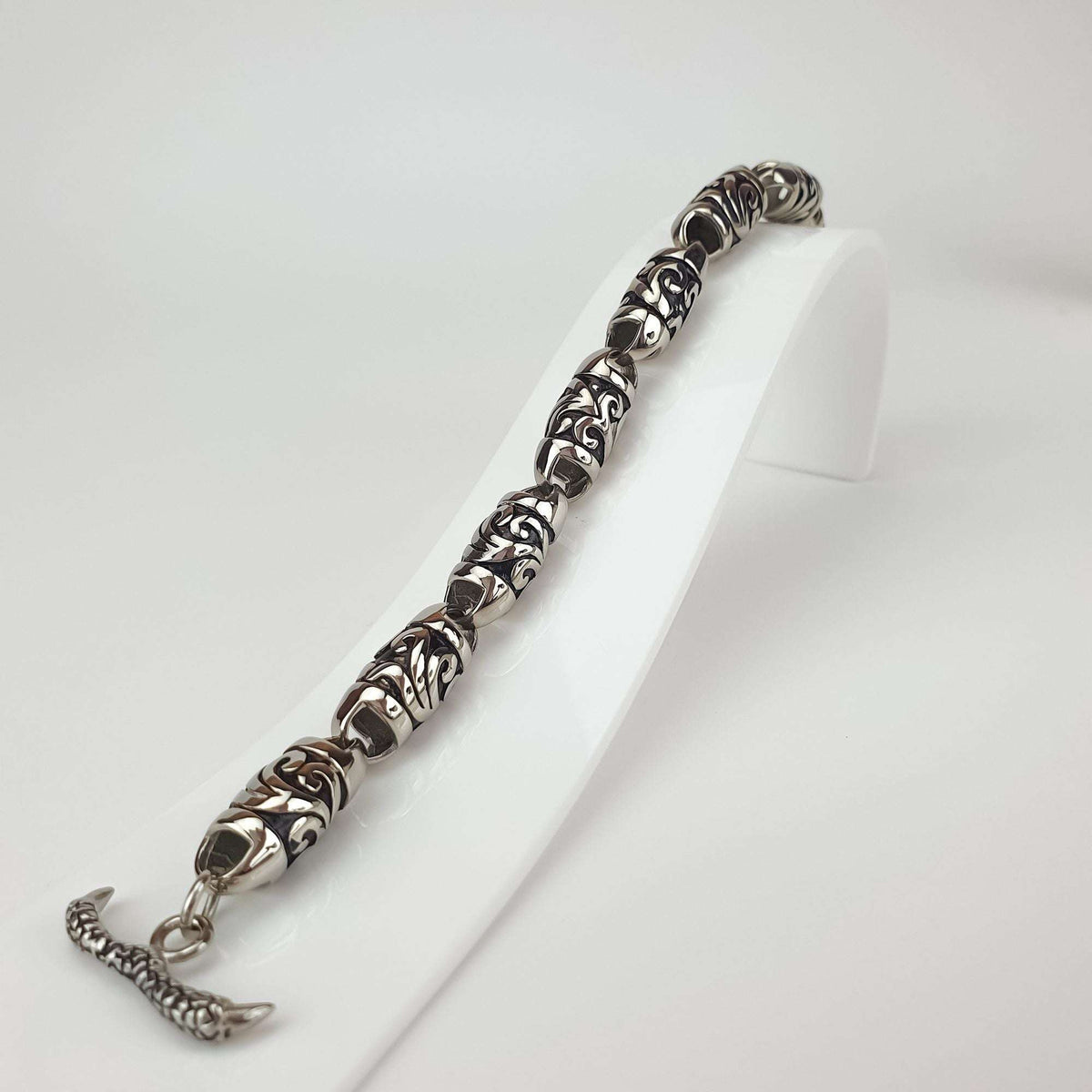 Bracelet close-up on a white stand, relief pattern and T-bar clasp visible