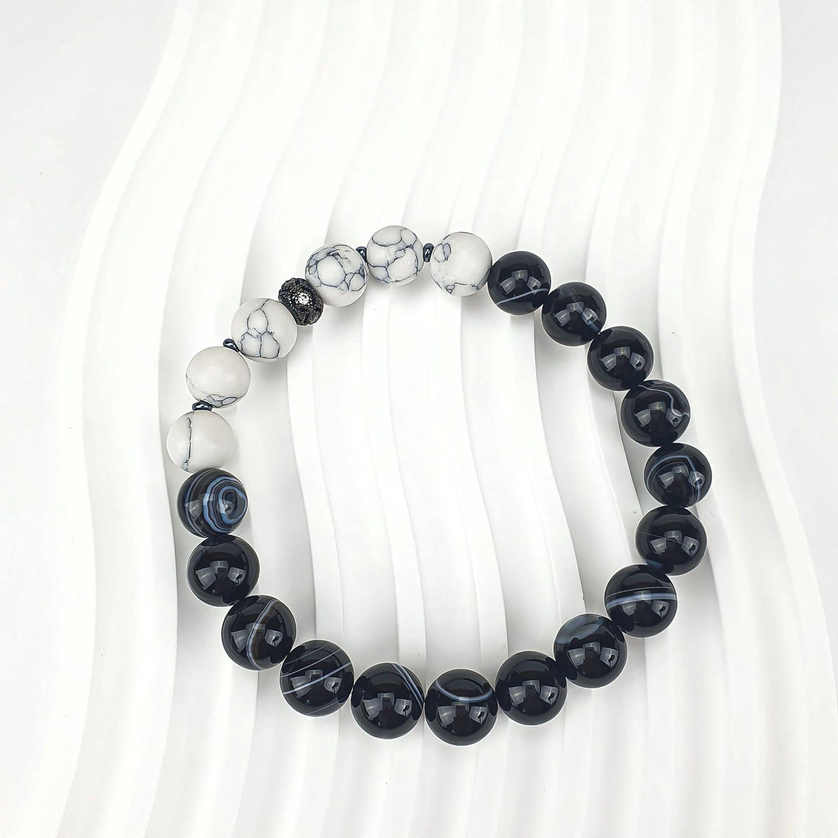 Bracelet on a wavy white background, glossy black and matt white beads