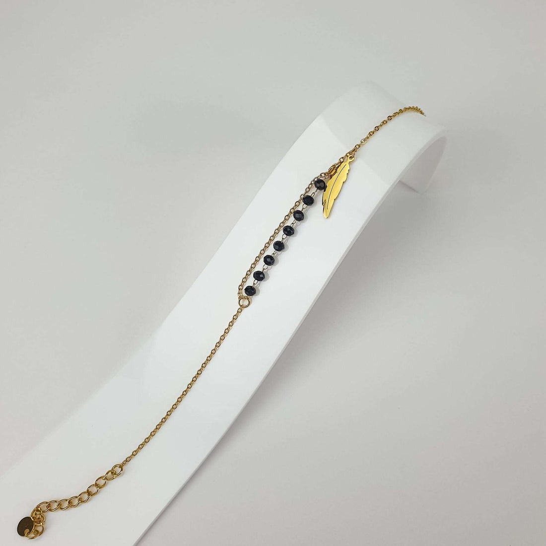 Feather charm bracelet at an angle on a white stand with black faceted beads