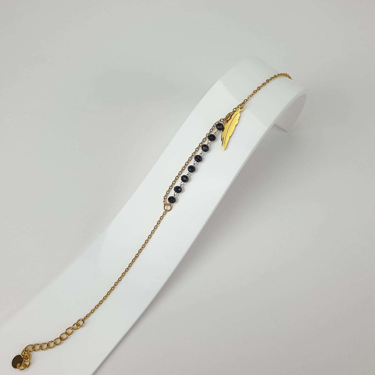 Feather charm bracelet at an angle on a white stand with black faceted beads