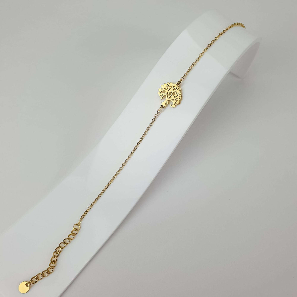 Delicate gold-plated tree of life bracelet stretched out on a white jewellery stand