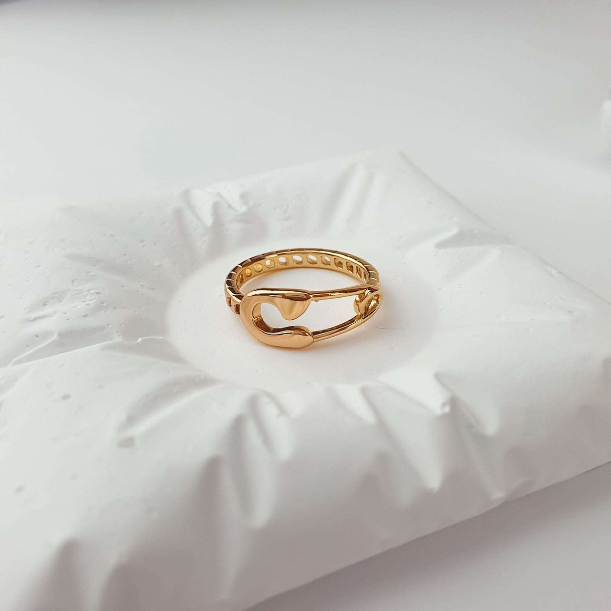 Safety pin ring at an angle on a white cushion, openwork band visible