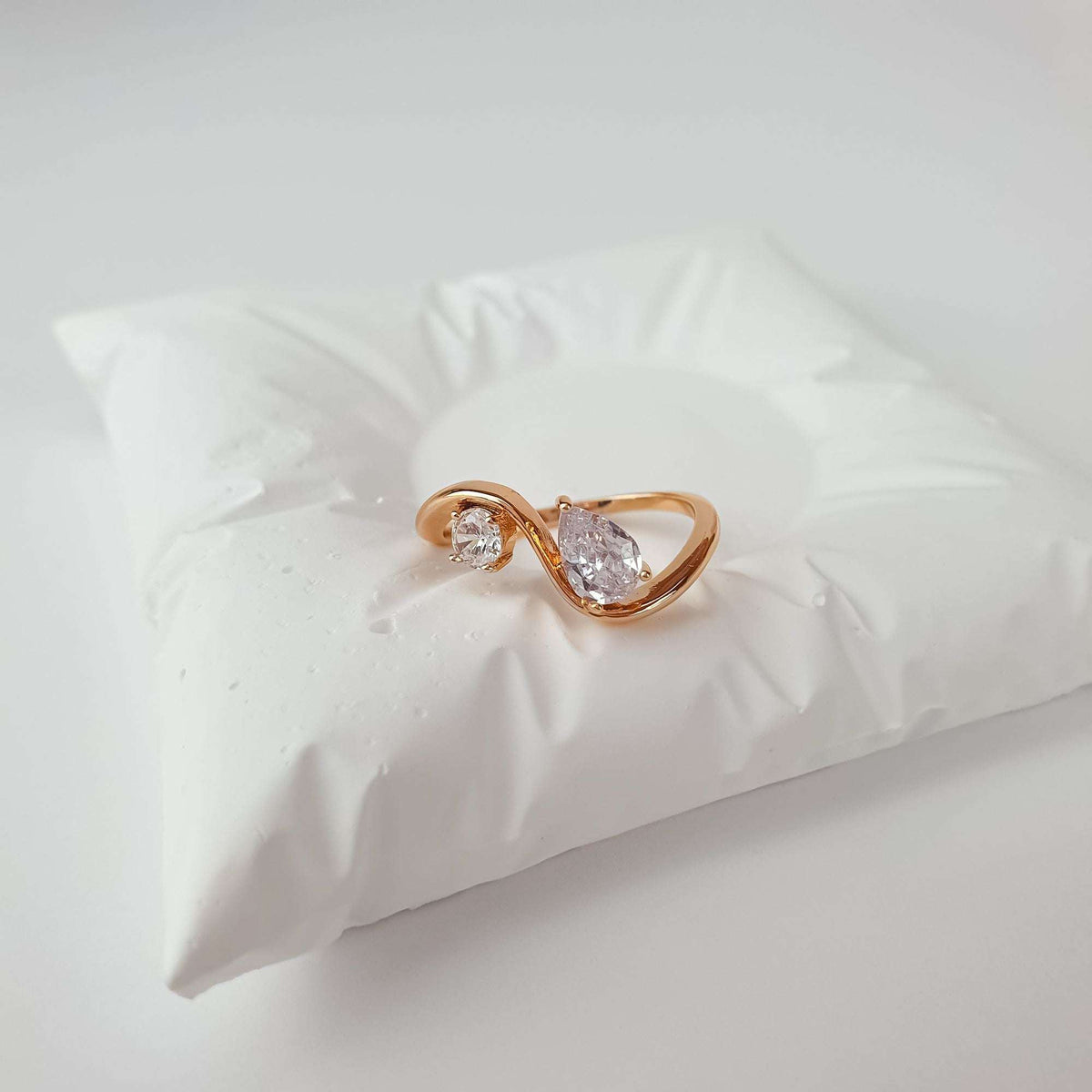 Two-stone gold-plated ring with round and teardrop crystals on a white cushion