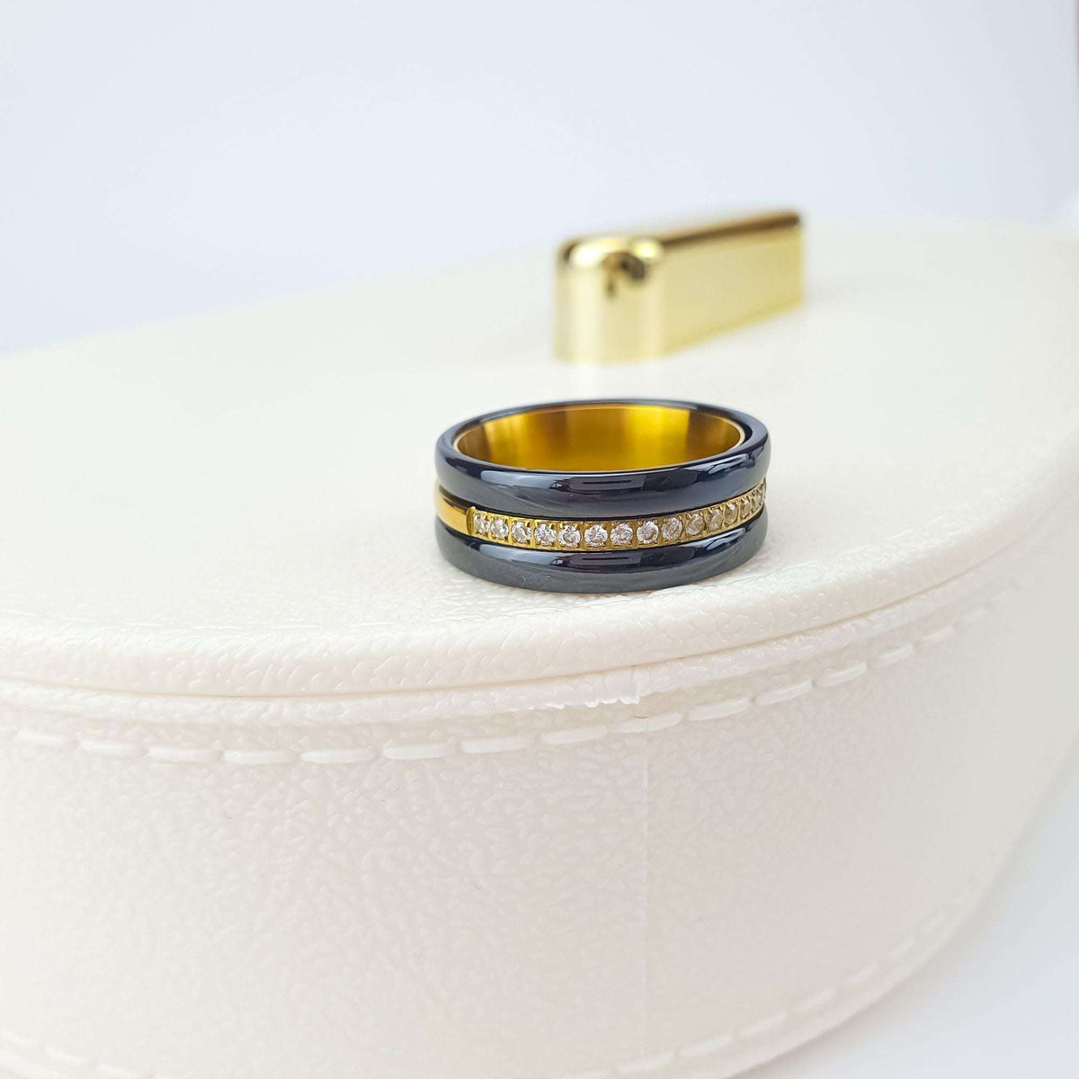 Black ceramic ring with cubic zirconia and gold-tone inside on a pale box