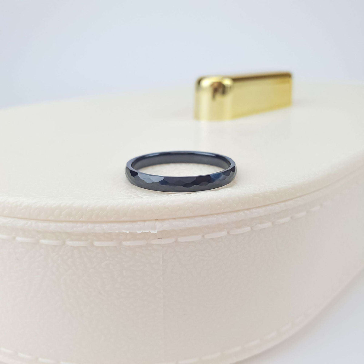Black ceramic ring with a multi-faceted surface on a cream jewellery box lid