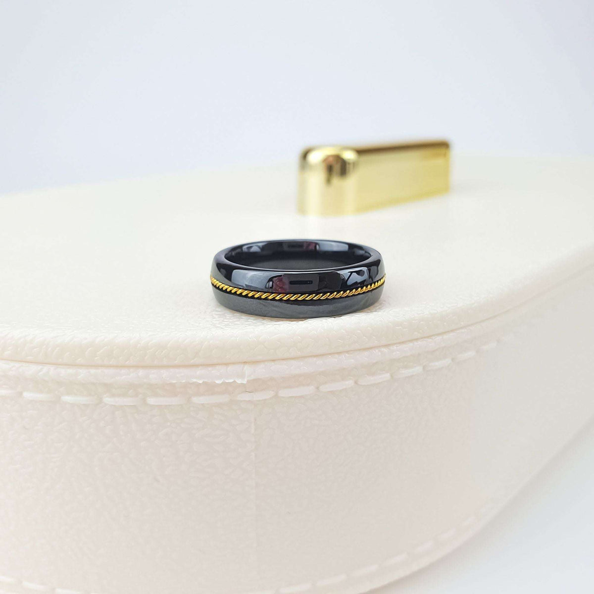 Black ceramic ring with gold-tone rope band standing on a cream jewellery box