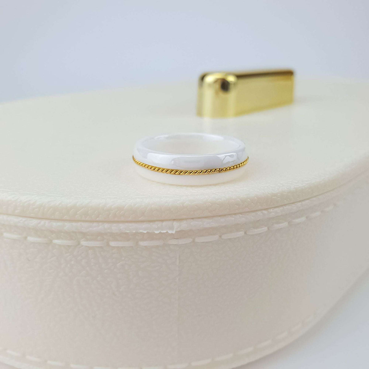 White ceramic ring with gold-tone rope, close-up on a cream jewellery box lid