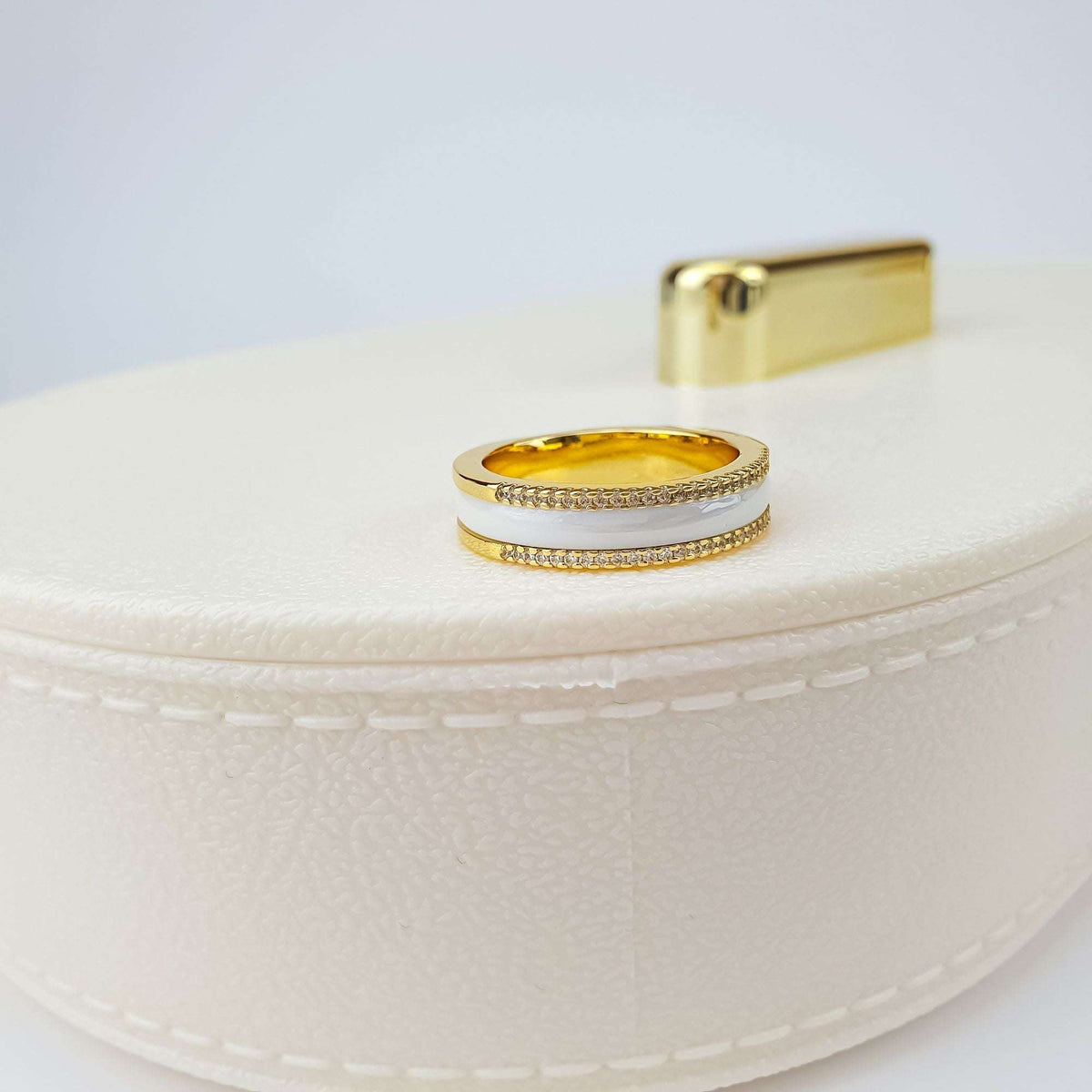 White ceramic ring with zirconia-set gold-tone edges standing on a cream jewellery box