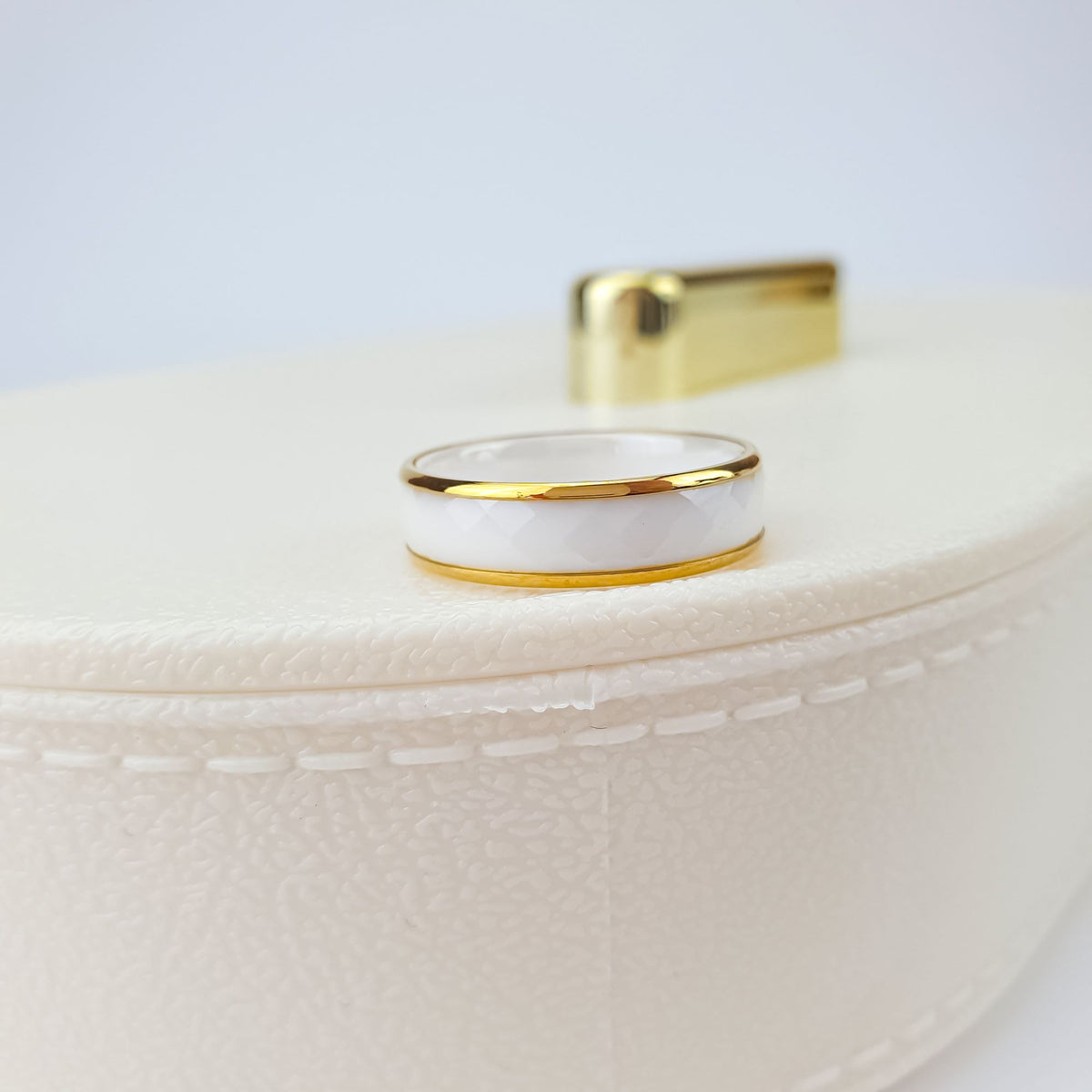 Faceted white ceramic ring with a shiny gold-tone rim on a jewellery box
