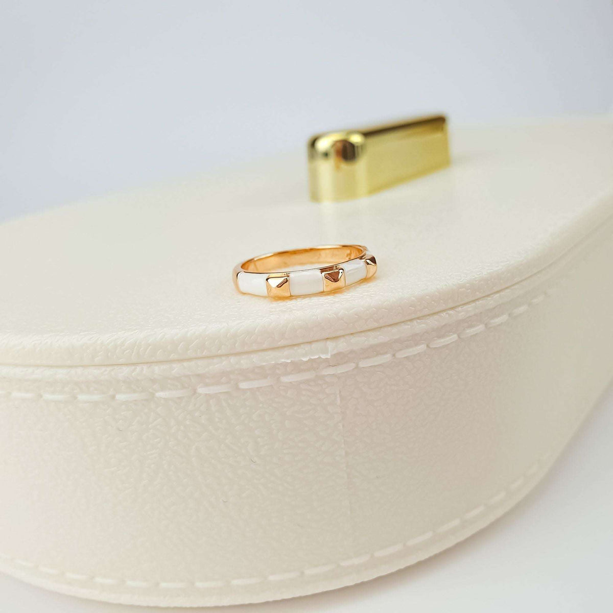 Gold-plated ring with white enamel segments, close-up on a cream jewellery box