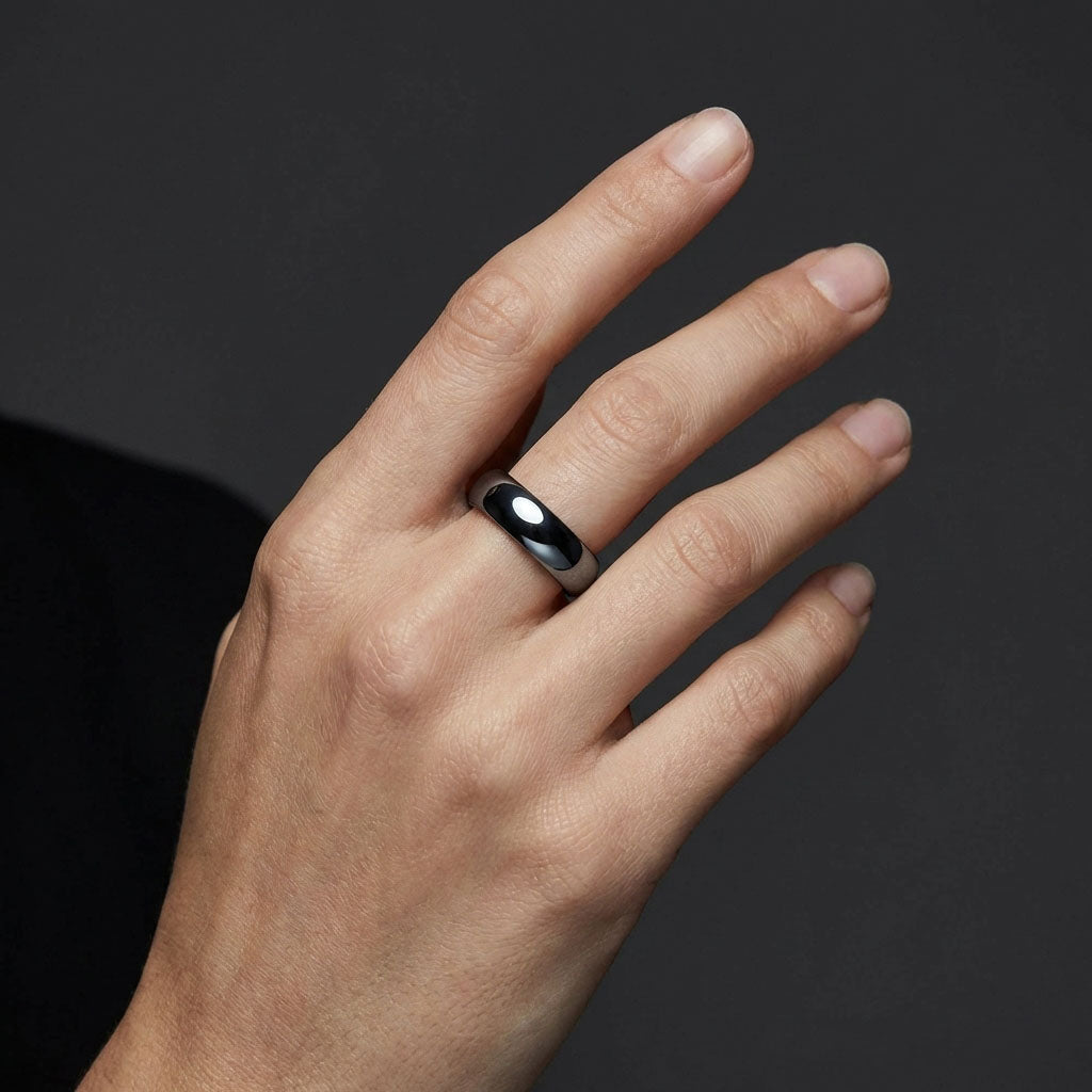 Rounded hematite ring on a man's hand against a dark grey studio background