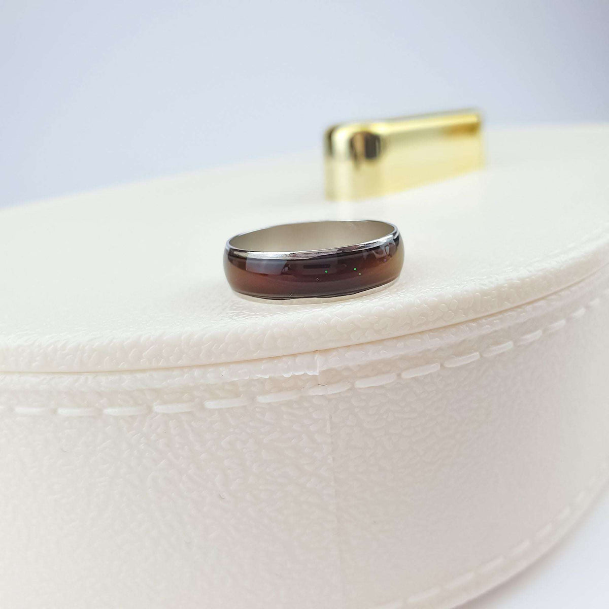 Dark brown mood ring with a shiny silver-tone rim on a light box