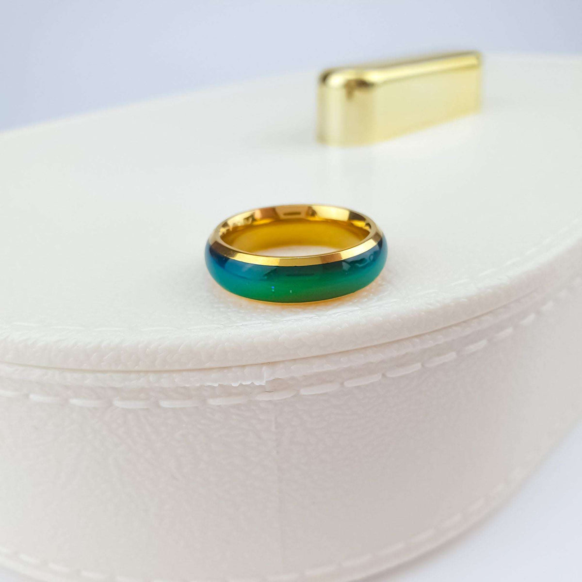 Blue green mood ring with a gold-plated rim on a white box