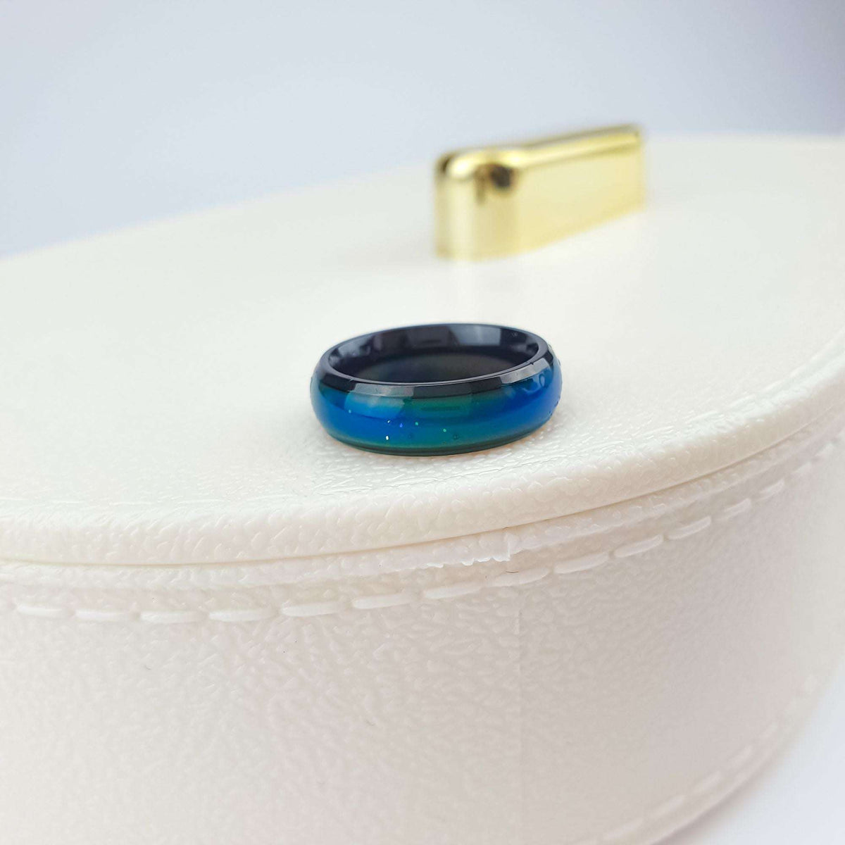 Mood ring with a dark frame and blue green surface on a white box