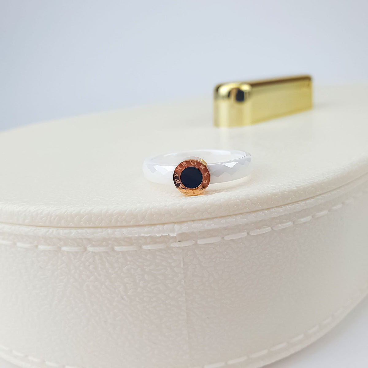 Close-up of the ceramic ring's gold-plated Roman numeral circle on a cream box