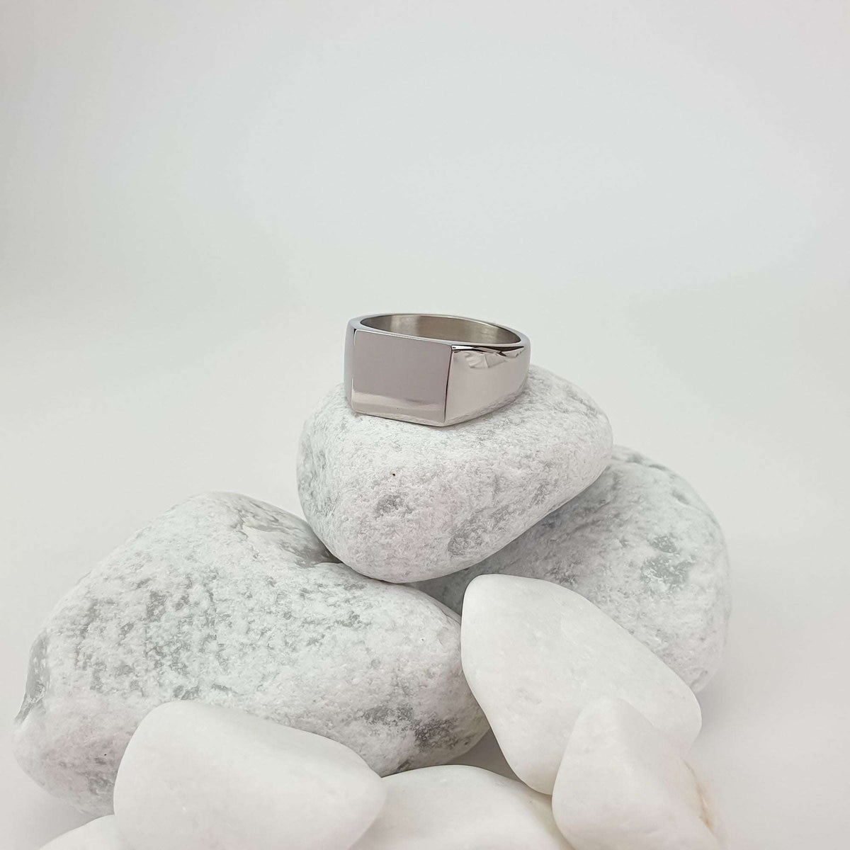 Steel signet ring with a rectangular plate on white pebbles, side view